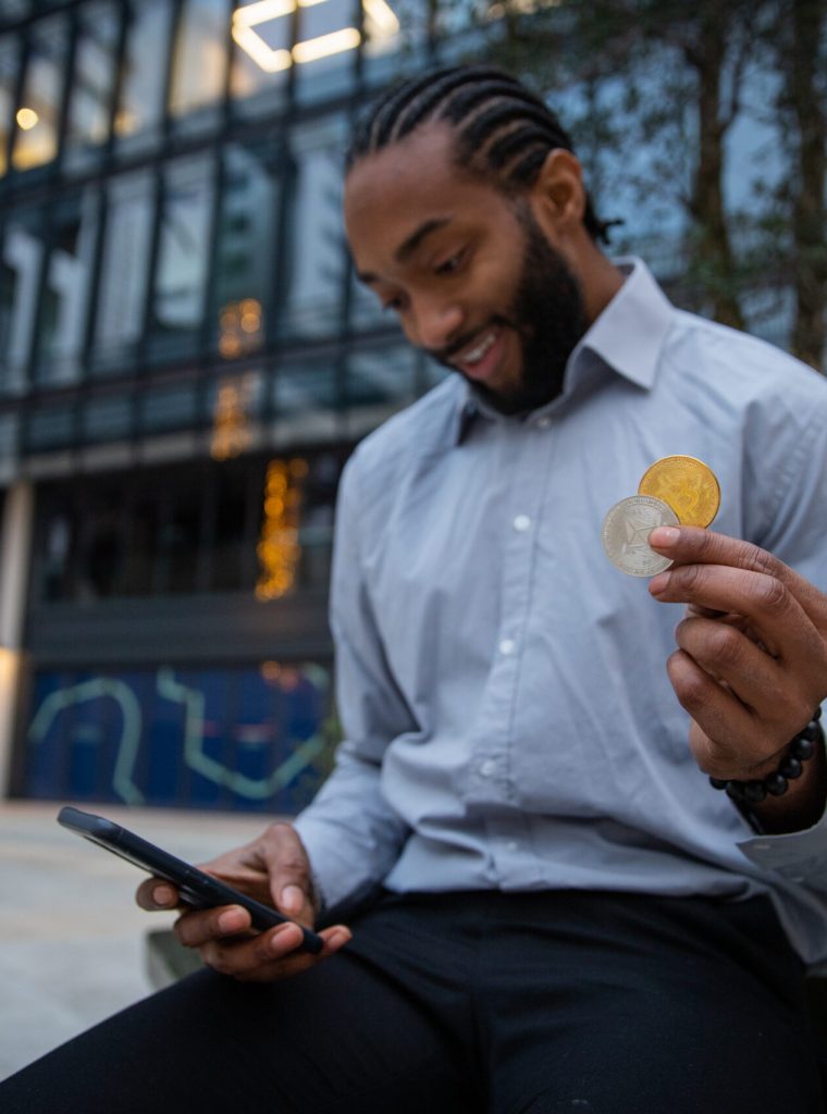 A cryptocurrency trader is happy with the results of his investments, he has his smartphone, a Bitcoin and ethereum coin in his hand